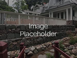 Front view of a home with a custom stone retaining wall and landscaped front yard featuring a rock garden and wooden handrails.